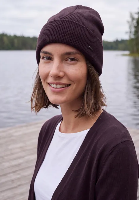 Jeune femme souriante en bonnet et gilet, posant au bord d'un lac.