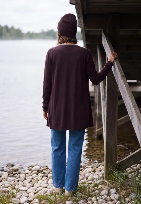 Vue de dos d'une personne en jean et gilet, appuyée sur un ponton au bord d'un lac.