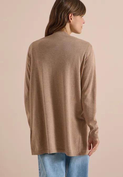 Rugaanzicht van een persoon in een beige cardigan en blauwe spijkerbroek tegen lichte achtergrond.