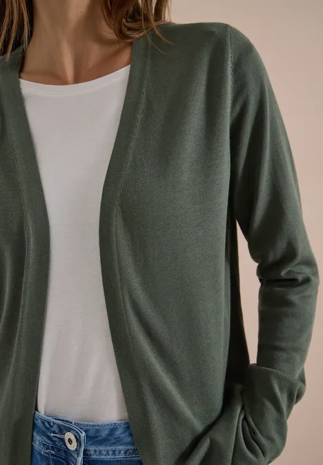 Eine Person trägt einen olivgrünen Cardigan über einem weißen T-Shirt.