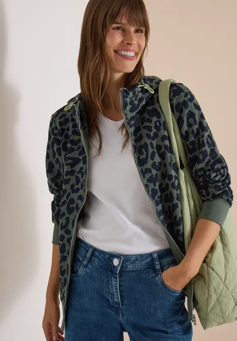 Sweatjacke mit Kapuze und Leo-Muster dried olive green Eine Frau trägt eine grüne Leo-Jacke, weißes T-Shirt, Jeans und lächelt.