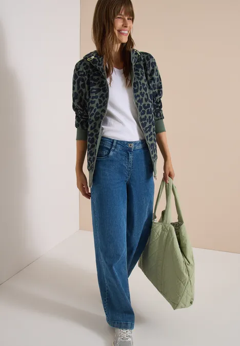 Sweatjacke mit Kapuze und Leo-Muster dried olive green Frau trägt Leopardenjacke, weißes T-Shirt, weite Jeans und hält eine grüne Tasche.