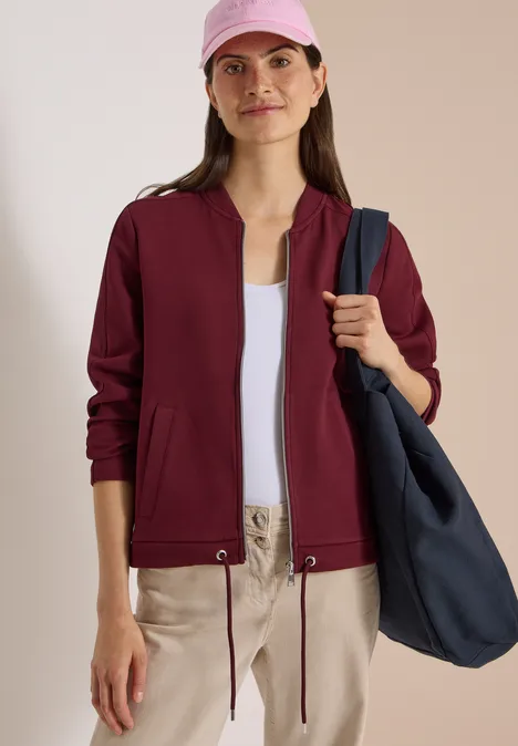 Sweat Blouson mit Tunnelzug red wine Frau in burgundfarbener Jacke, weißem Top, beiger Hose, rosa Mütze und großer blauer Tasche.