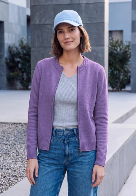 Cardigan zippé à manches longues et col rond pastel lilac melange Frau mit lila Cardigan, grauem Top, Jeans und blauer Schirmmütze steht im Freien.