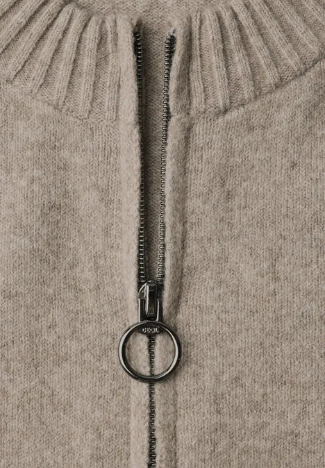 Detailaufnahme eines beigefarbenen Strickpullovers mit Reißverschluss und runder Zipperlasche.