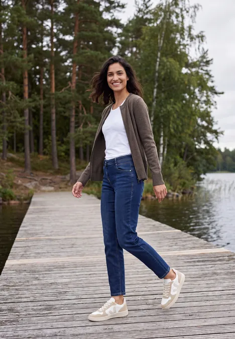 Langarm Cardigan mit Rundhals und Zipper mushroom taupe melange Eine Frau in Jeans, weißem Top und Strickjacke spaziert lächelnd auf einem Steg am See mit Wald im Hintergrund.