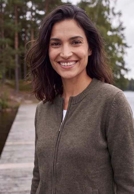 Langarm Cardigan mit Rundhals und Zipper mushroom taupe melange Frau mit braunem Pullover steht lächelnd auf einem hölzernen Steg vor einem ruhigen See und Wald im Hintergrund.