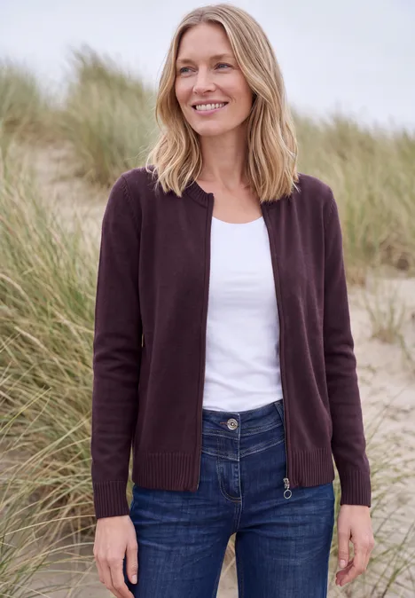 Langarm Cardigan mit Rundhals und Zipper eggplant red melange Frau im lila Cardigan und Jeans steht lächelnd in Dünen mit Strandgras.