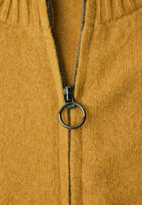 Nahaufnahme eines senfgelben Strickpullovers mit mittig geschlossenem Reißverschluss und rundem Ringanhänger