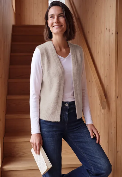 Offene Federgarn-Weste in Unifarbe cashmere beige Eine lächelnde Frau in Jeans und Weste steht an einer Holztreppe und hält ein Buch.