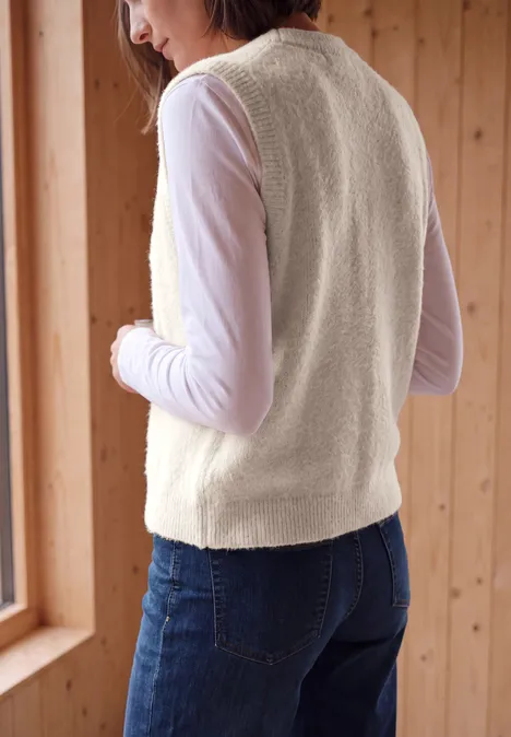 Offene Federgarn-Weste in Unifarbe cashmere beige Frau von hinten in beige Fleece-Weste und weißem Langarmshirt vor einem Fenster in Holzraum.