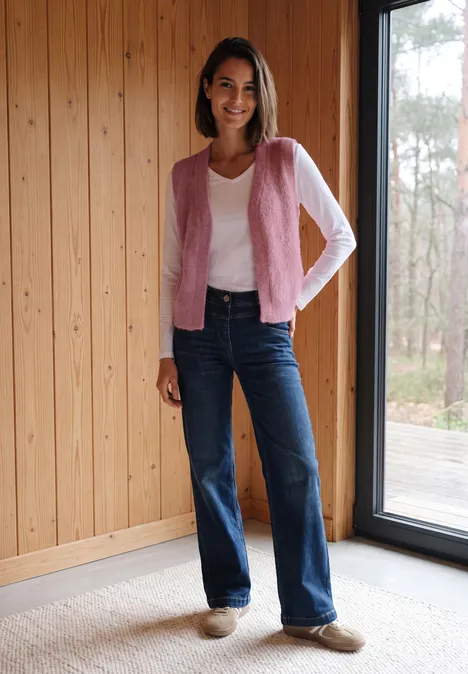 Open vest van veergaren in effen kleur velvet rose Frau mit rosa Cardigan, weißem Shirt und Jeans steht in Holzraum vor Fenster.
