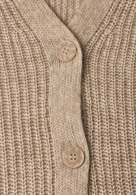 Gros plan sur un cardigan beige à grosse maille avec deux boutons en bois.