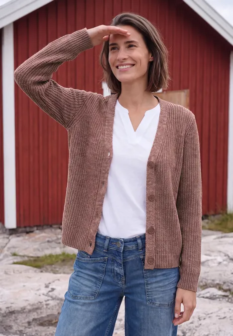 Chunky Cardigan mit V-Neck und Melange-Optik dark russet red melange Eine lächelnde Frau in Jeans und brauner Strickjacke steht vor einem roten Haus und blickt in die Ferne.