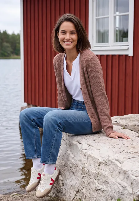 Chunky Cardigan mit V-Neck und Melange-Optik dark russet red melange Eine lächelnde Frau in Jeans und Strickjacke am Wasser vor einem roten Haus.