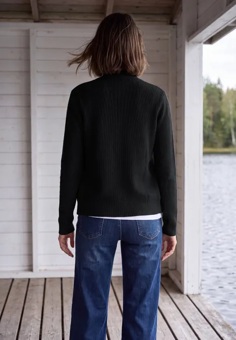 Cardigan mit Stehkragen und Zipper Black Person steht mit dem Rücken zur Kamera, trägt schwarzen Pullover und blaue Jeans auf Holzsteg am See.