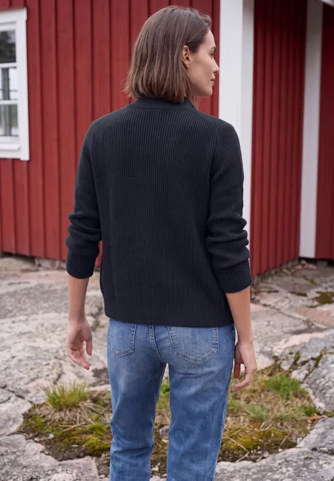 Cardigan mit Stehkragen und Zipper urban dark blue Eine Frau steht mit dem Rücken zur Kamera in Jeans und schwarzem Pullover vor einem roten Holzhäuschen.