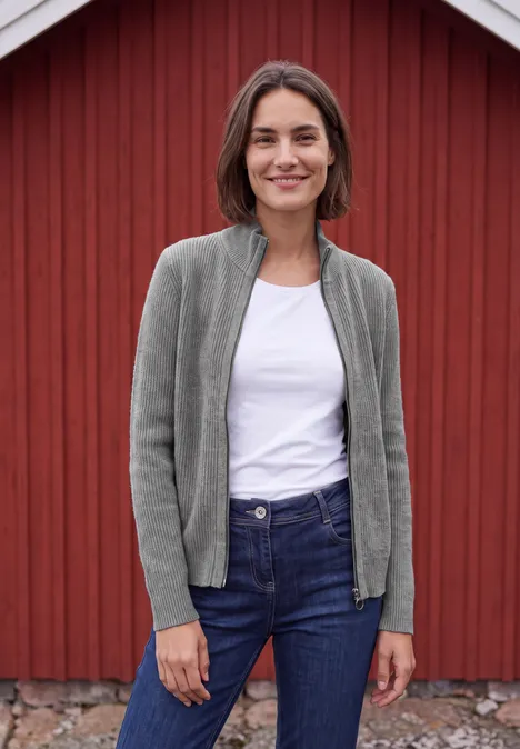 Cardigan mit Stehkragen und Zipper sporty grey melange Eine Frau steht vor einer roten Holzwand und trägt weißen T-Shirt, graue Strickjacke und blaue Jeans.