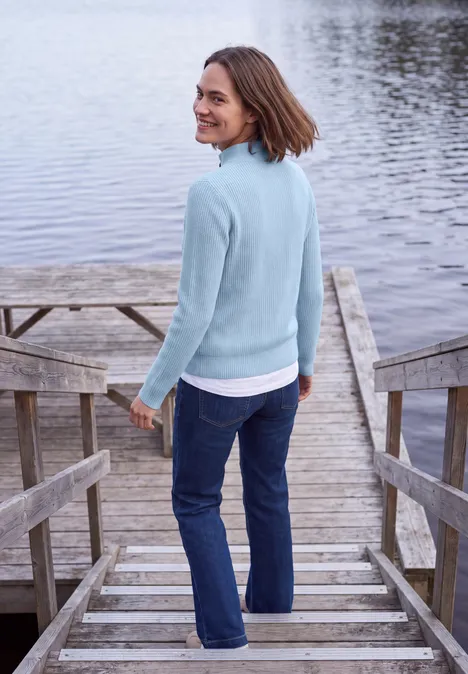 Cardigan mit Stehkragen und Zipper cosmopolitan blue Eine Frau im hellblauen Pullover und Jeans steht auf einem Steg und blickt zurück auf das Wasser.