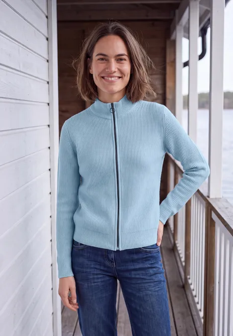 Cardigan mit Stehkragen und Zipper cosmopolitan blue Eine lächelnde Frau steht auf einer Veranda, trägt einen hellblauen Reißverschluss-Pullover und Jeans.