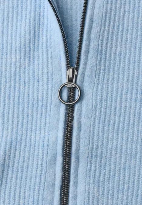 Cardigan mit Stehkragen und Zipper cosmopolitan blue Nahaufnahme eines Reißverschlusses mit rundem Zugring auf hellblauem Cordstoff.