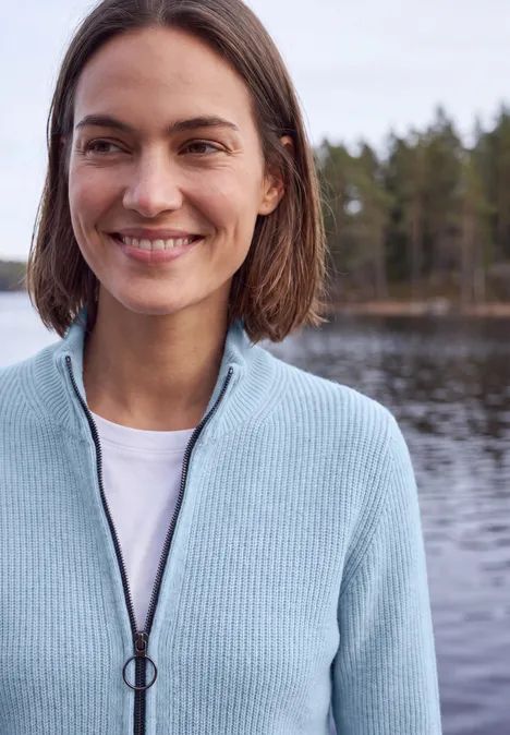 Cardigan mit Stehkragen und Zipper cosmopolitan blue Lächelnde Frau mit kurzem braunem Haar, hellblauem Cardigan vor einem See und Wald im Hintergrund.