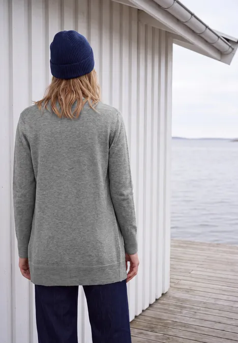 Langer Cardigan in offener Passform sporty grey melange Person mit grauem Pullover und blauer Mütze steht rückwärts auf Holzsteg am Wasser.