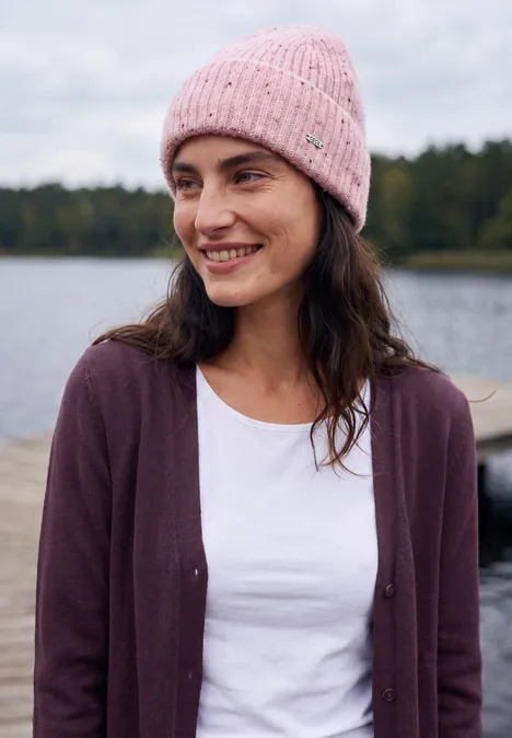 Langer Cardigan in offener Passform eggplant red melange Junge Frau in rosa Mütze lächelt am Ufer eines Sees.