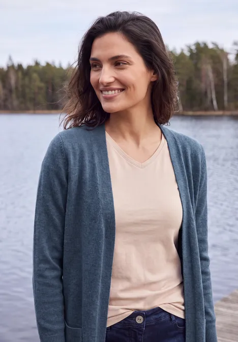 Cardigan long à la coupe ample cotton blue melange Une femme souriante sur un quai au bord d'un lac, vêtue d’un cardigan et d’un t-shirt clair.