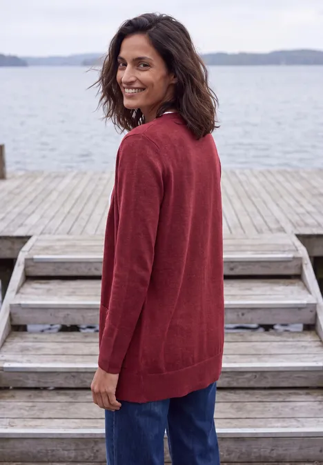 Langer Cardigan in offener Passform rhubarb melange Eine Frau in rotem Cardigan und Jeans steht lächelnd auf einem Holzsteg am Wasser.
