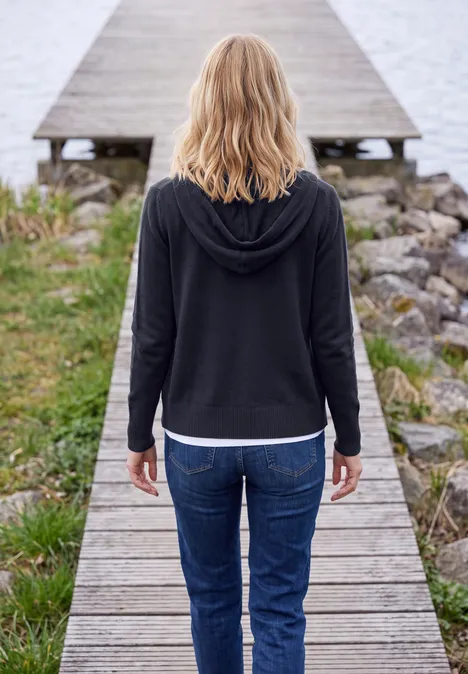 Junge Frau steht rücklings auf einem Holzsteg und blickt aufs Wasser.