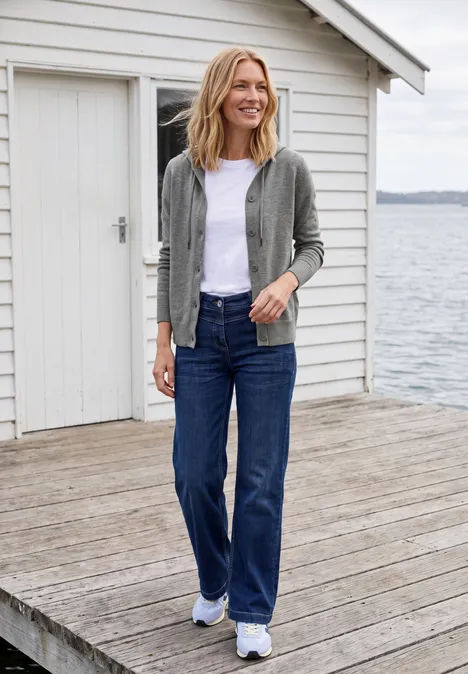 Langarm Cardigan mit Kapuze sporty grey melange Lächelnde Frau steht auf hölzernem Steg am See, trägt lässige Jacke, weißes T-Shirt, weite Jeans und Sneakers.