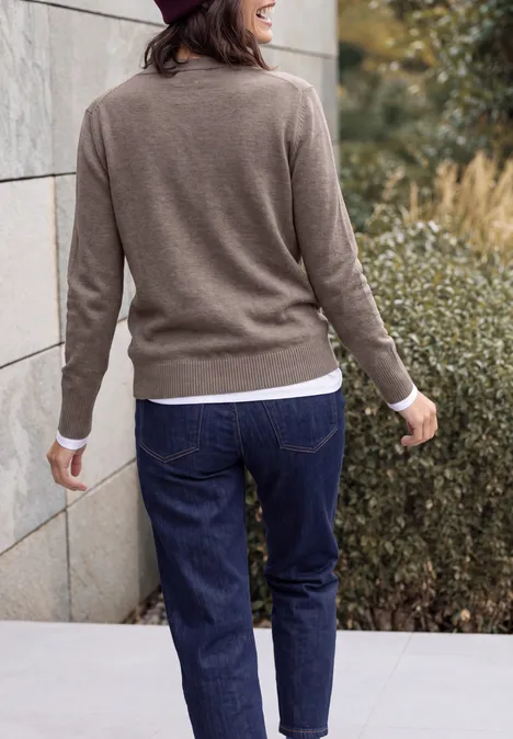 Vrouw van achteren in jeans en beige trui wandelt buiten.