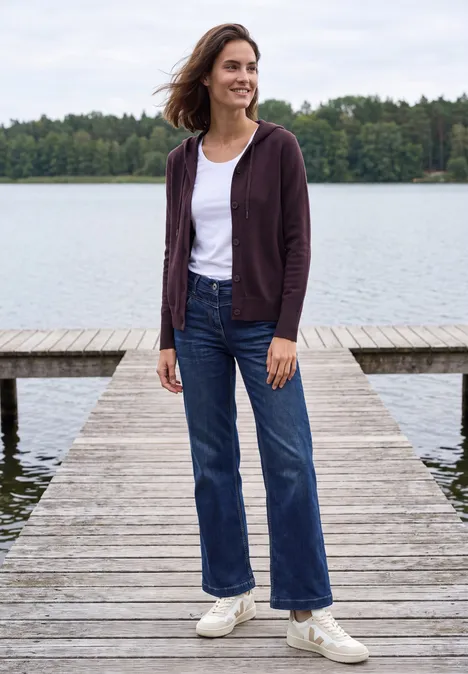 Langarm Cardigan mit Kapuze eggplant red melange Frau in weißem T-Shirt, lila Hoodie und Jeans steht lächelnd auf einem Steg am See.