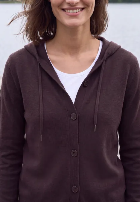 Langarm Cardigan mit Kapuze eggplant red melange Lächelnde Frau in braunem Kapuzenpullover und weißem Shirt vor unscharfem Hintergrund.