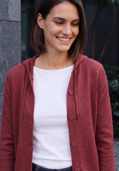 Frau mit kurzem braunen Haar, roter Kapuzenjacke und weißem T-Shirt lächelt entspannt.