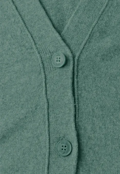 Close-up van een groene gebreide cardigan met knopen en V-hals.