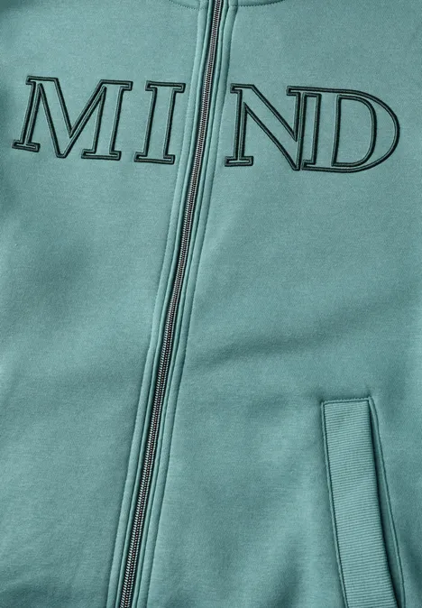 Zbliżenie turkusowej bluzy z kapturem na zamek z nadrukiem „MIND” na przodzie.