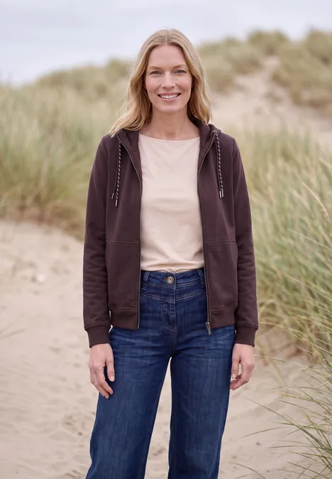 Sweatjacke mit Zipper und Kapuze berry red Eine lächelnde Frau in brauner Kapuzenjacke und Jeans steht auf Dünen mit Strandgras im Hintergrund.