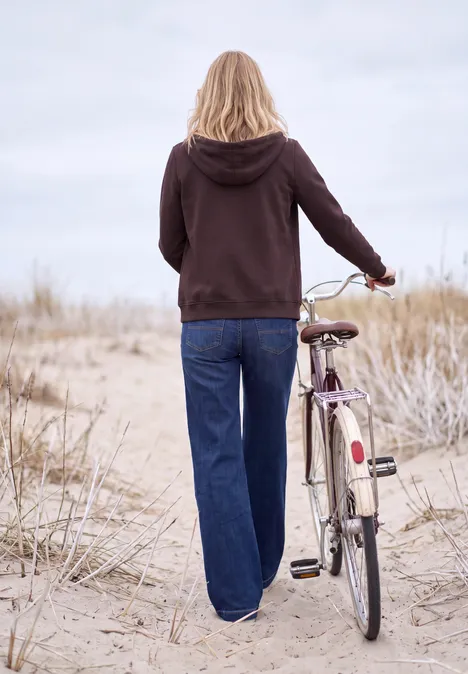 Sweatjacke mit Zipper und Kapuze berry red Eine Person im Kapuzenpullover schiebt ein Fahrrad über sandige Dünen am Strand.