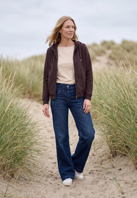 Sweatjacke mit Zipper und Kapuze berry red Eine Frau spaziert lächelnd in Jeans und Kapuzenjacke über sandige Dünen