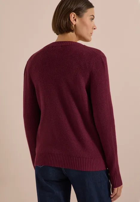 Eine Frau von hinten trägt einen weinroten Pullover und blaue Jeans.