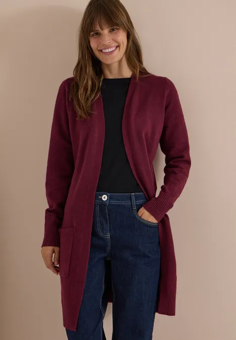Langer Cardigan in offener Passform red wine Frau lächelt, trägt einen bordeauxfarbenen Cardigan, schwarzes Shirt und Jeans vor neutralem Hintergrund.
