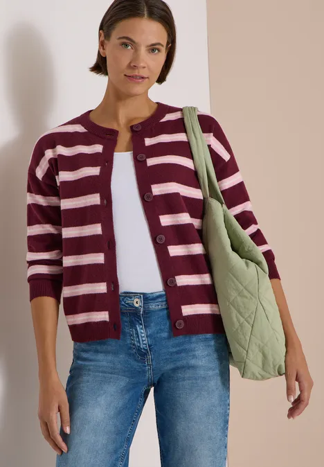 Frau trägt gestreifte Strickjacke, Jeans und grüne gesteppte Tasche.
