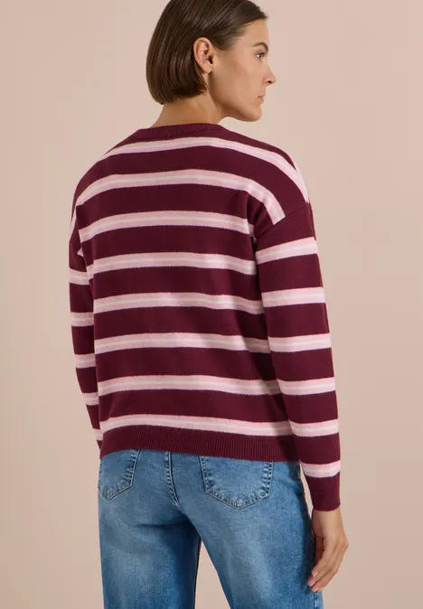 Frau in dunkelrotem-weiß gestreiftem Pullover und Jeans, Rückenansicht, vor hellem Hintergrund.