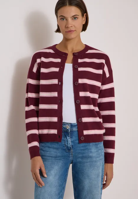 Frau in gestreifter Strickjacke in Bordeaux und Rosa, unterlegt mit weißem Shirt, kombiniert mit Jeans.
