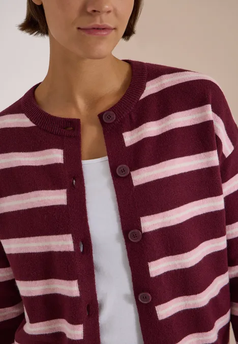 Teilansicht einer Frau in burgund-rosa gestreiftem Cardigan über weißem Top.