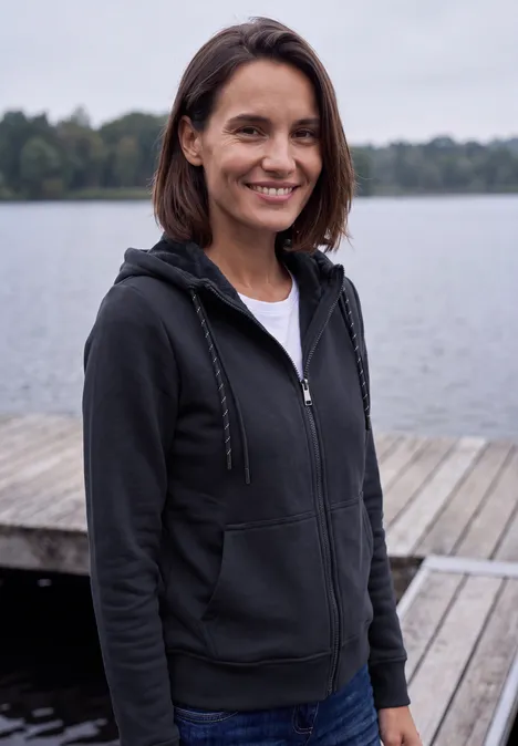Langarm Sweatjacke mit Kapuze urban dark blue Eine junge Frau in Kapuzenjacke steht auf einem Steg am See und lächelt in die Kamera.
