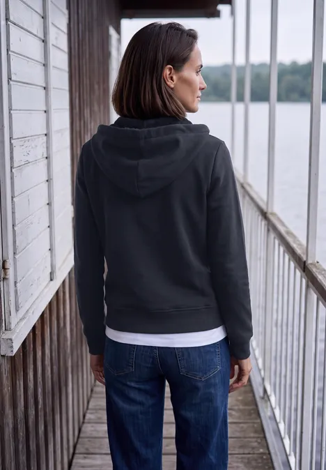 Langarm Sweatjacke mit Kapuze urban dark blue Frau in schwarzer Kapuzenjacke und Jeans steht auf hölzernem Steg und blickt aufs Wasser.