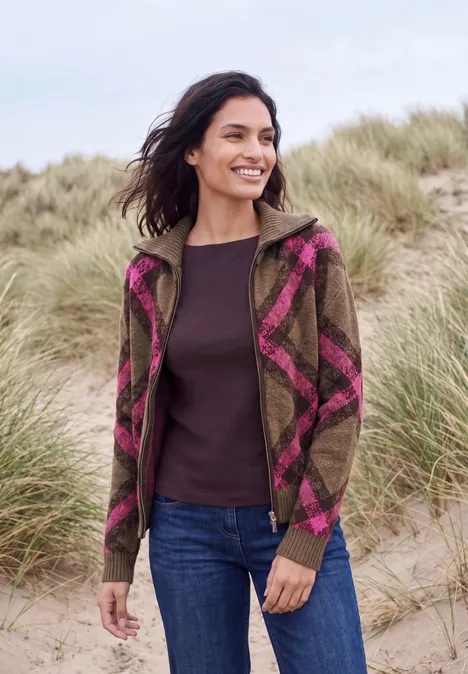 Federgarn Cardigan mit Troyerkragen pink flash Frau in kariertem Hoodie und Jeans steht lächelnd in Dünenlandschaft.